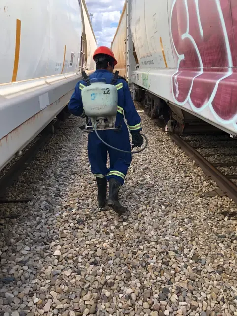 Worker spraying vegetation along rail cars at industrial facility
